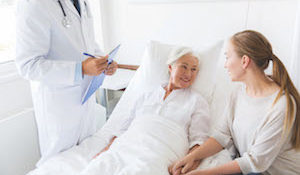 medicine, healthcare and people concept - senior woman patient with daughter and doctor with clipboard at hospital ward