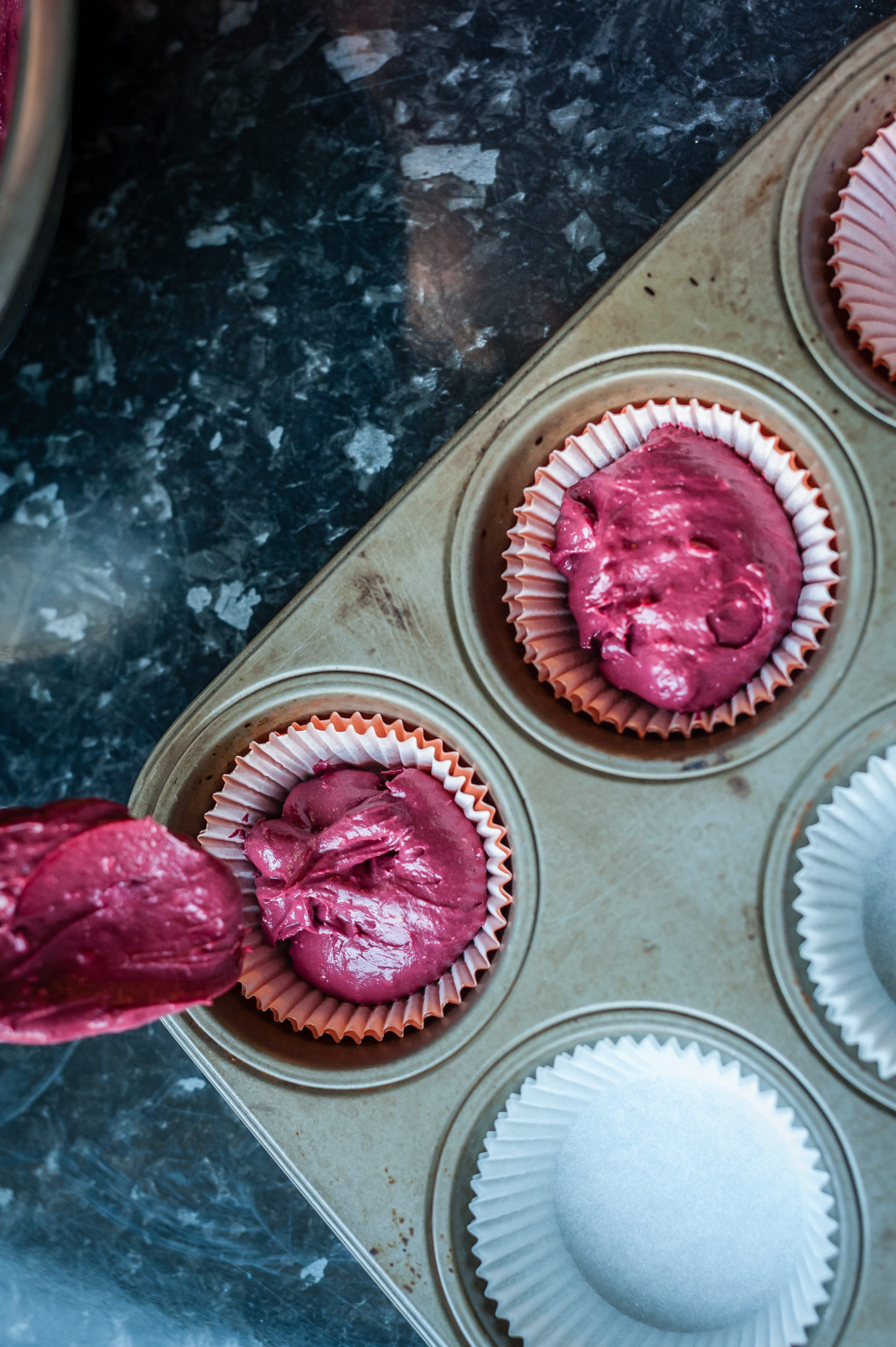 Spoon pouring dough into molds for muffins. Process of cupcakes preparation. Homemade Red Velvet Cupcakes. Close up, soft focus. The Scoop | Cherry Cupcakes and Dark Chocolate Granola 2