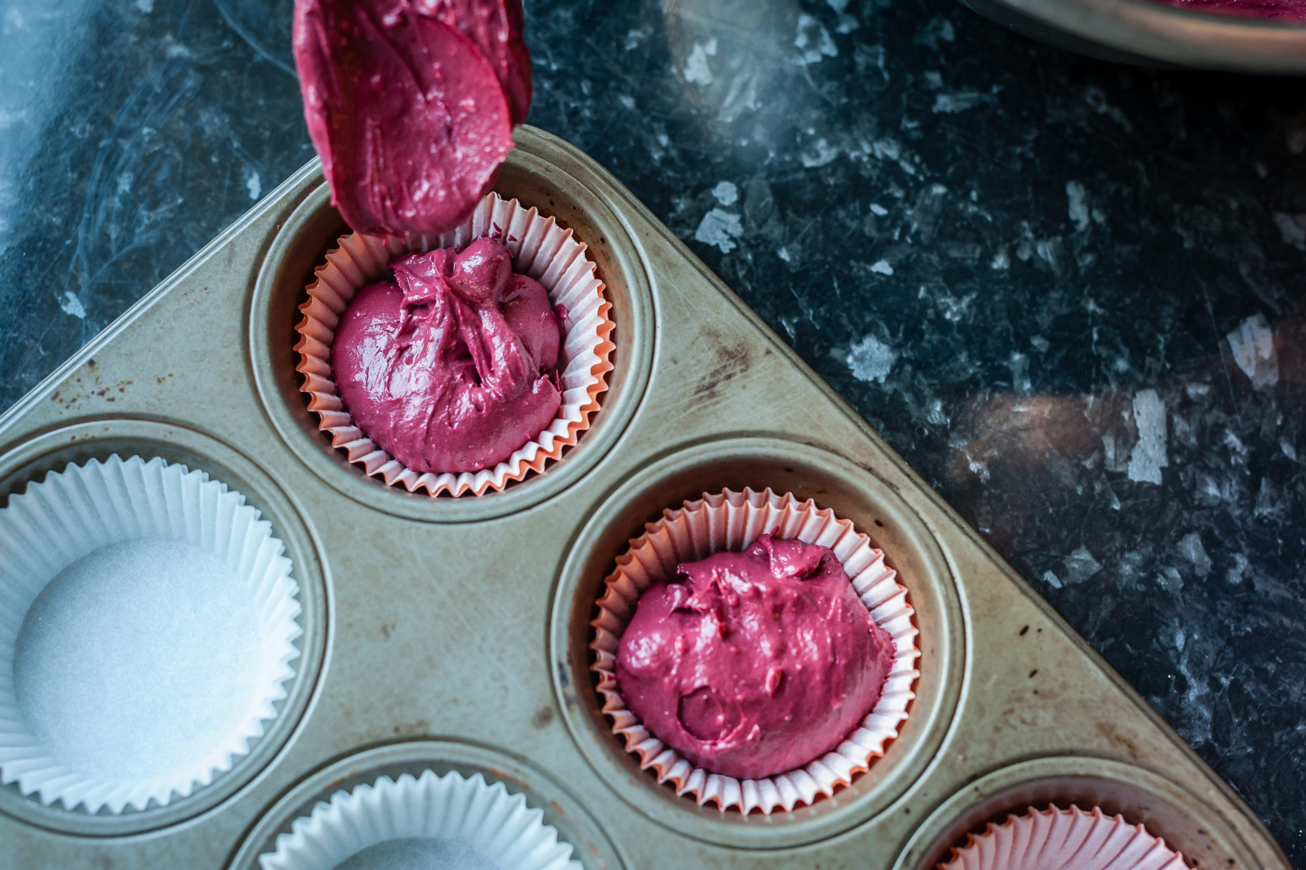 Spoon pouring dough into molds for muffins. Process of cupcakes preparation. Homemade Red Velvet Cupcakes. Close up, soft focus.